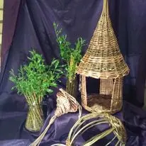 Basketry pieces and a small woven structure displayed with greenery